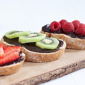 Toast topped with Sweet Freedom Choc Pot chocolate spread and fresh fruit, 3 slices, on has strawberries on top, on has kiwi fruit and one has raspberries